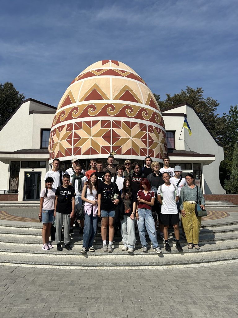A group photo of teenagers standing outside in front of a giant decorative egg.