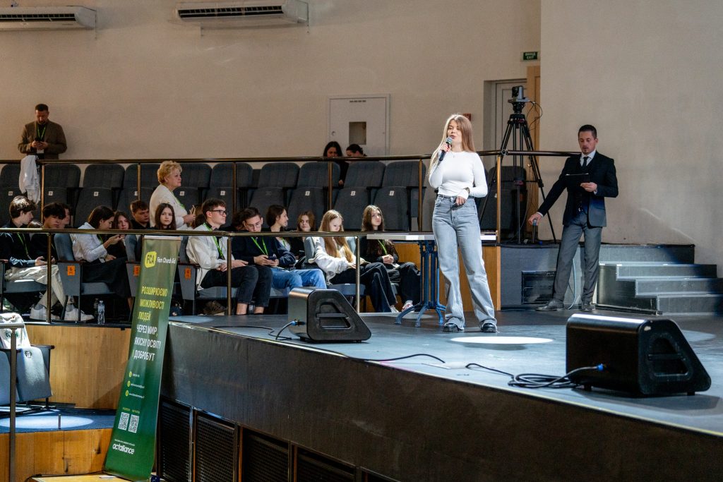A young woman stands on a stage and speaks into a microphone