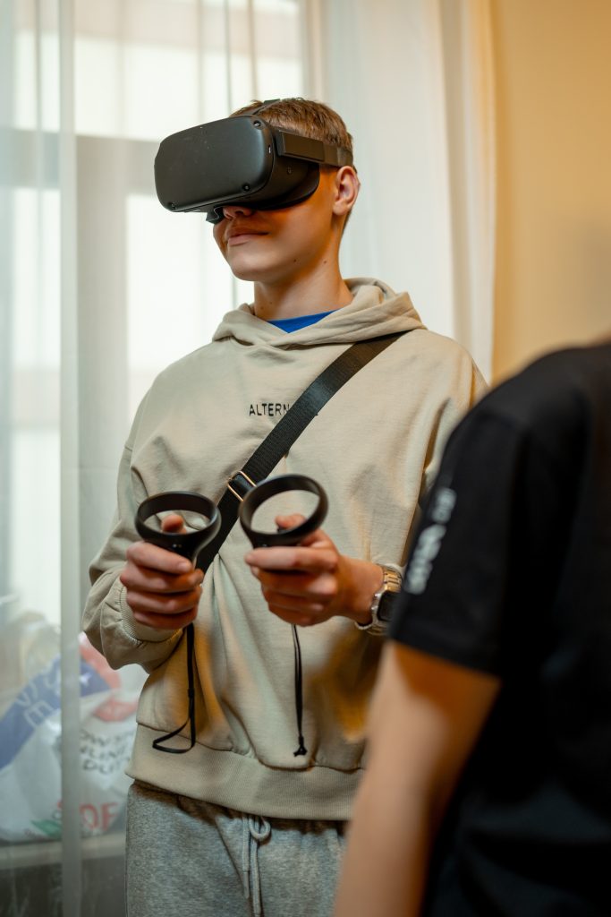 A young person wears a VR headset and uses joysticks to control what they see.