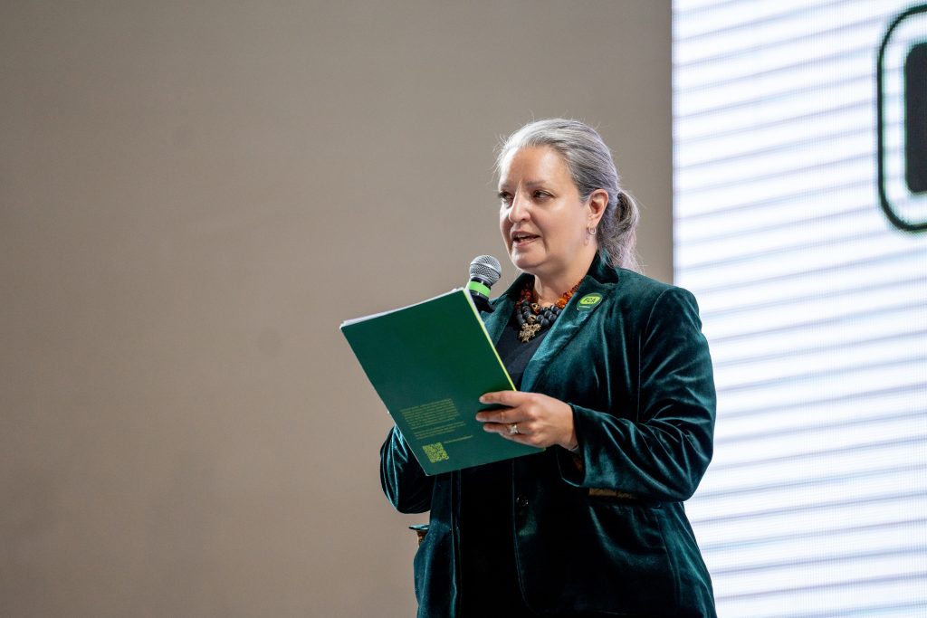 A woman holding an FCA branded document speaks into a microphone