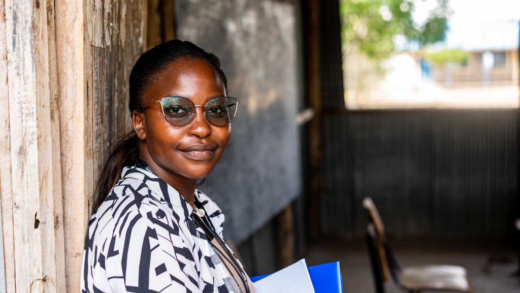 Nainen katsoo kameraan kenialaisen pakolaisalueen koulun luokkahuoneen ovella.