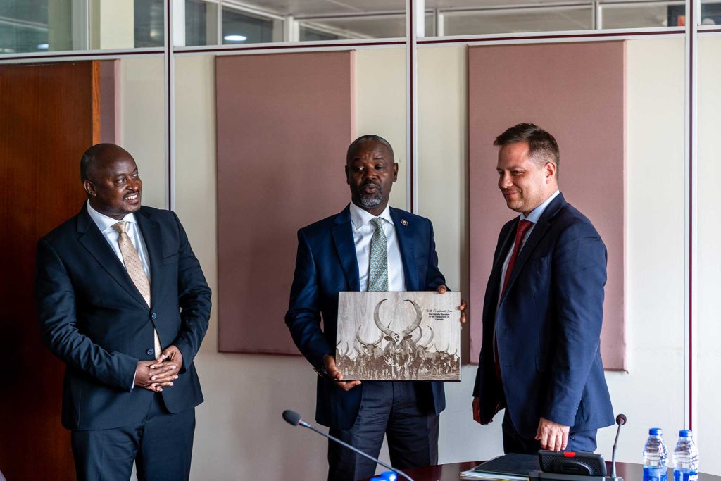 Kolme miestä seisoo yhdessä. Keskimmäinen mies pitelee käsissään taulua.