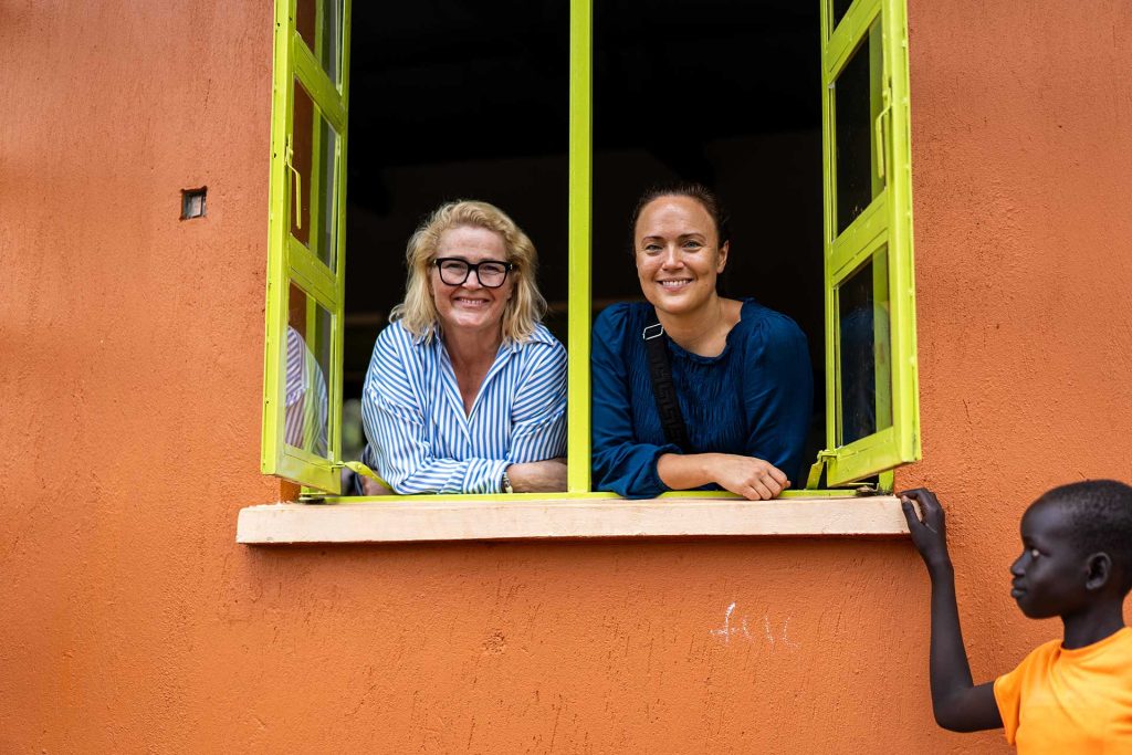 Kaksi naista katsoo ulos koulurakennuksen ikkunasta. Ikkunan ulkopuolella naisia katsoo lapsi.