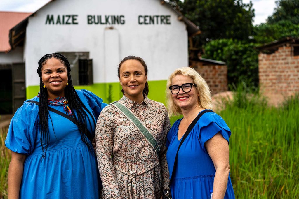 Kolme suomalaista kansanedustajaa poseeraa iloisesti kameralle ison rakennuksen edessä.