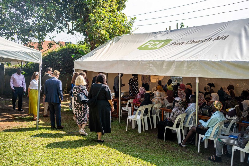 Telttakatoksen alle on kerääntynyt istumaan ihmisiä. Myös teltan ulkopuolella seisoo ihmisiä.