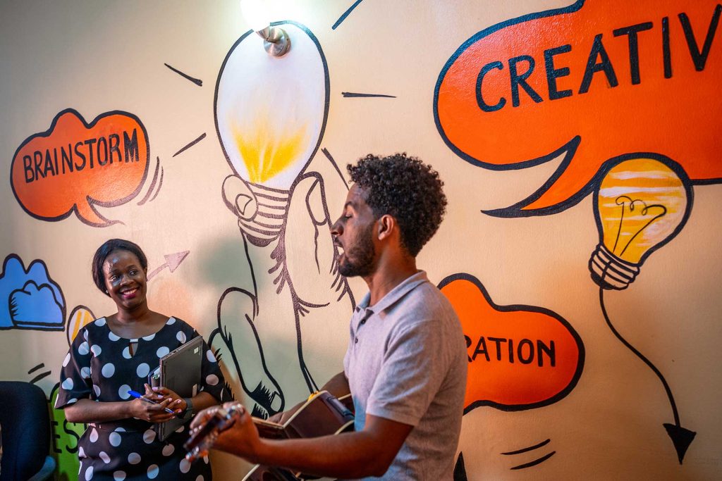 Kaksi henkilöä keskustelee. Takana olevaan seinään on maalattu värikkäitä, puhekuplia esittäviä kuva.