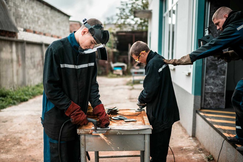 Nuoret miehet hitsaavat ulkona pöydän ääressä. 