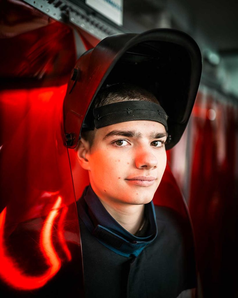 Hitsausmaskin otsalleen nostanut poika katsoo kameraan. 