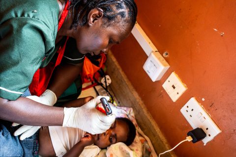 A nurse bends over a baby and takes a reading from a small device.