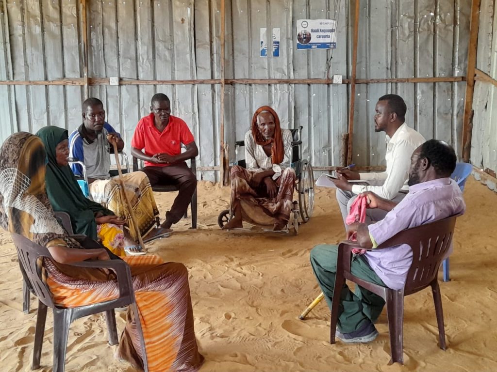 A group of people, one with a wheelchair, one with a walking stick, sit in a circle talking.