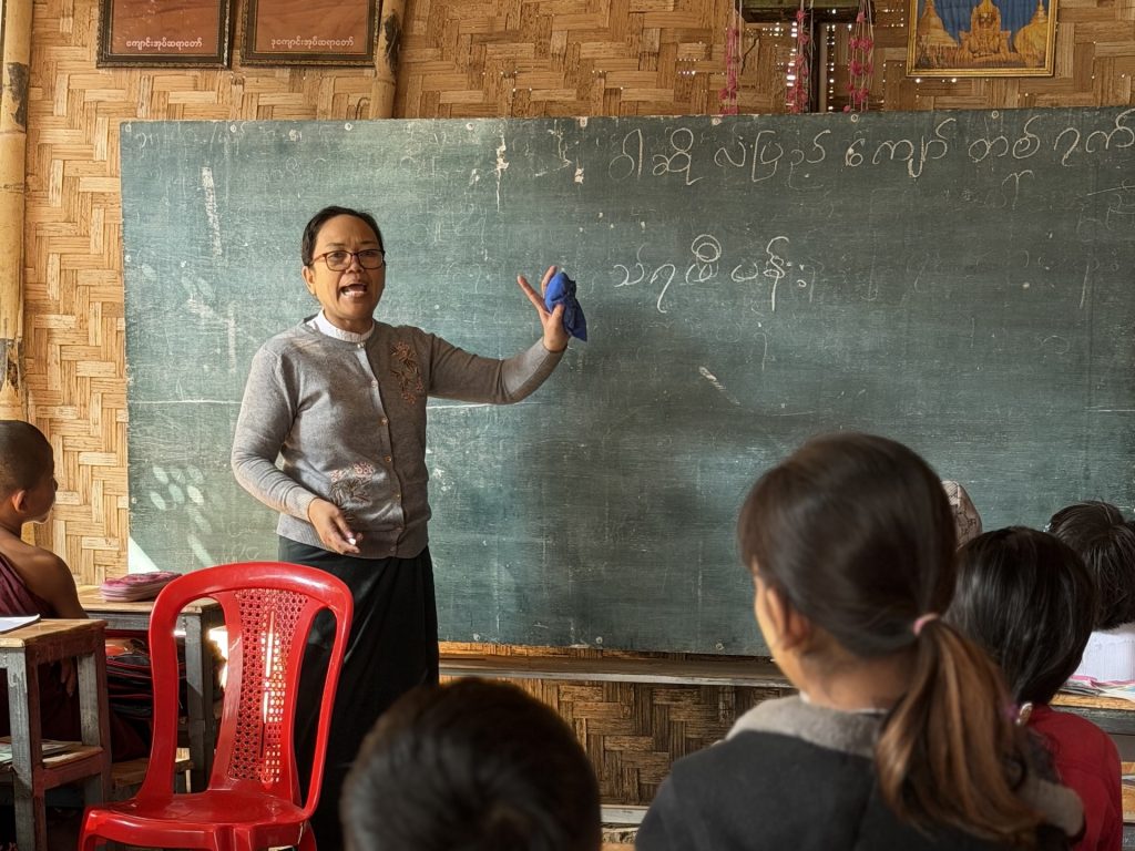A woman standing in front of a blackboard teaches in a classroom to children.