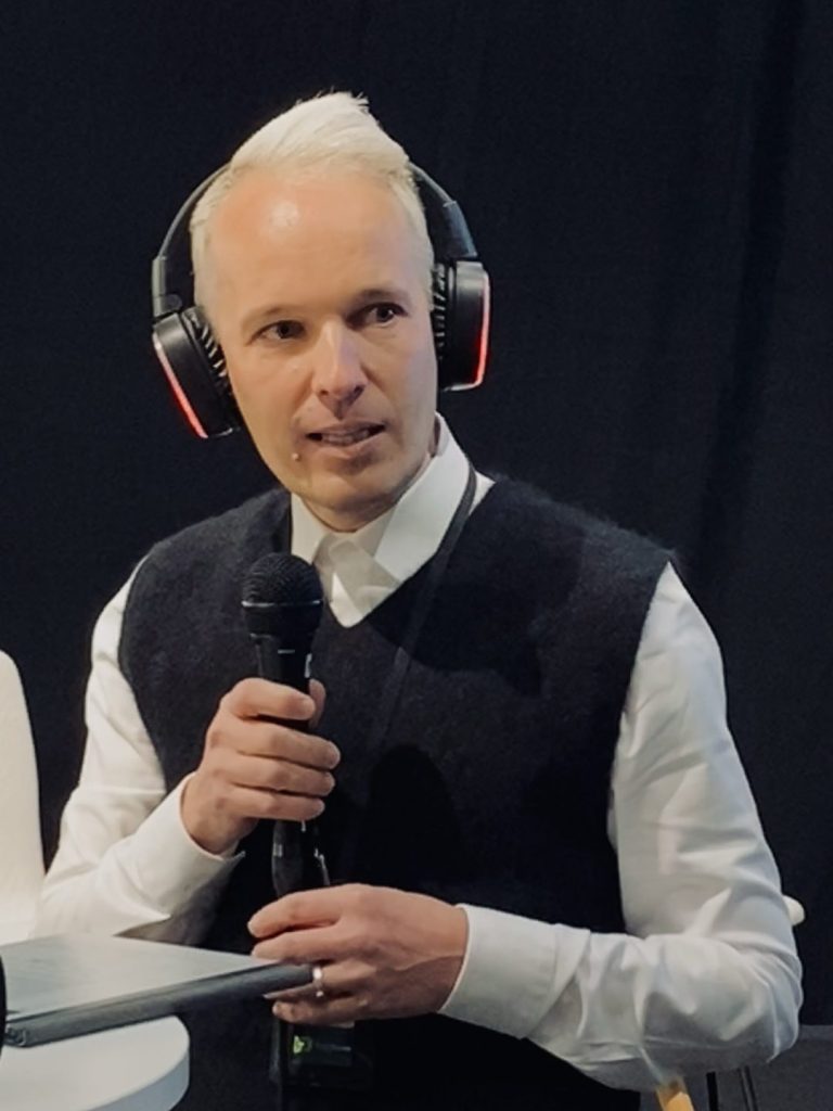 A man in headphones sits listening with a microphone in his hand