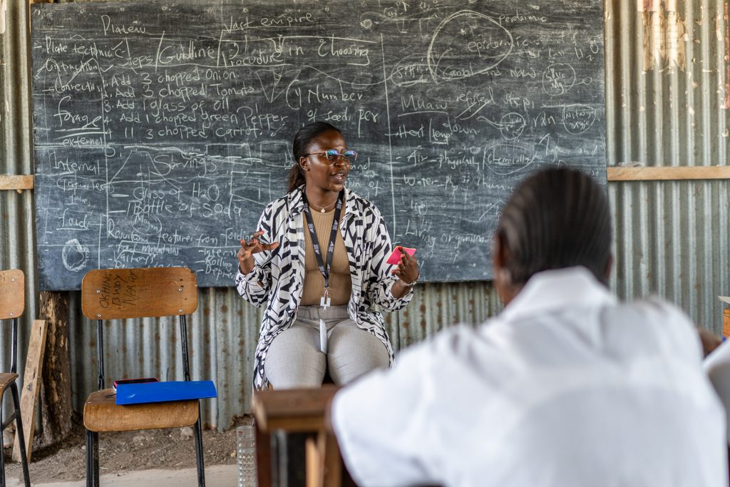 A teacher sits in front of a blackboard talks to a listening student