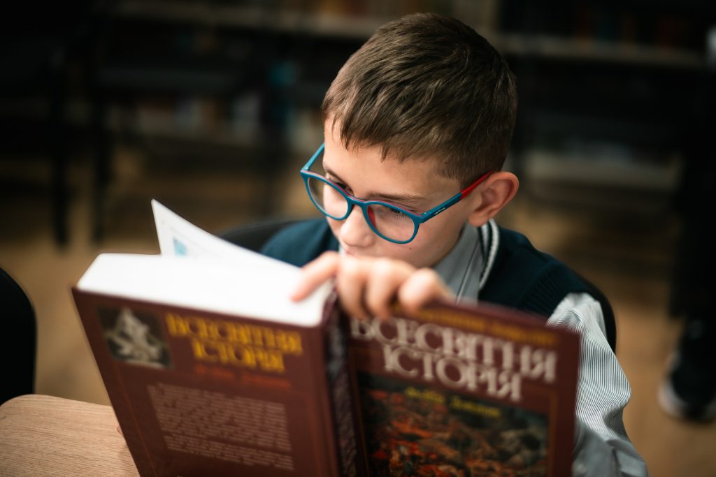 A schoolboy wearing glasses is engrossed in a book.