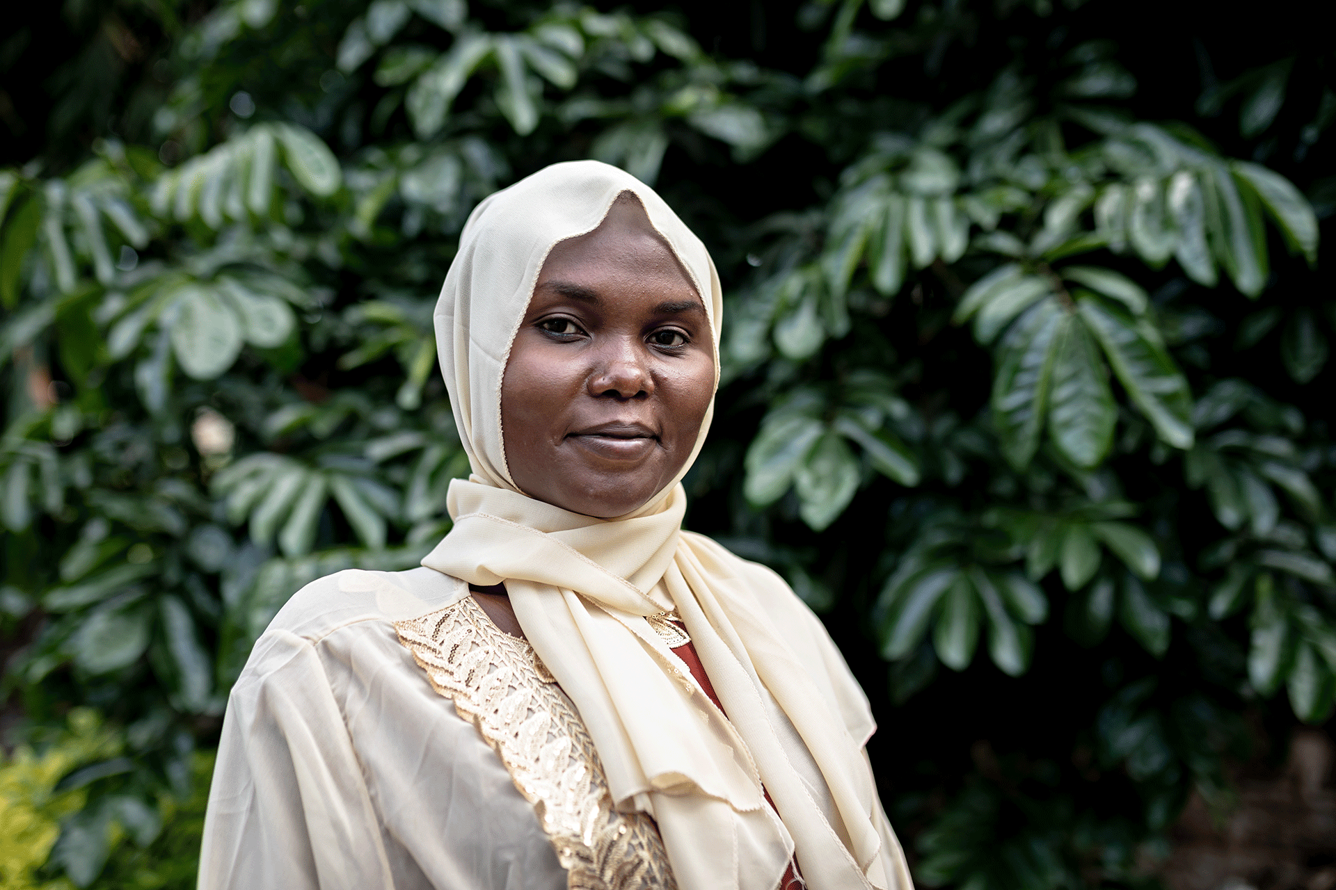 Nainen valkoinen huivi päässään vihreän puun edessä.