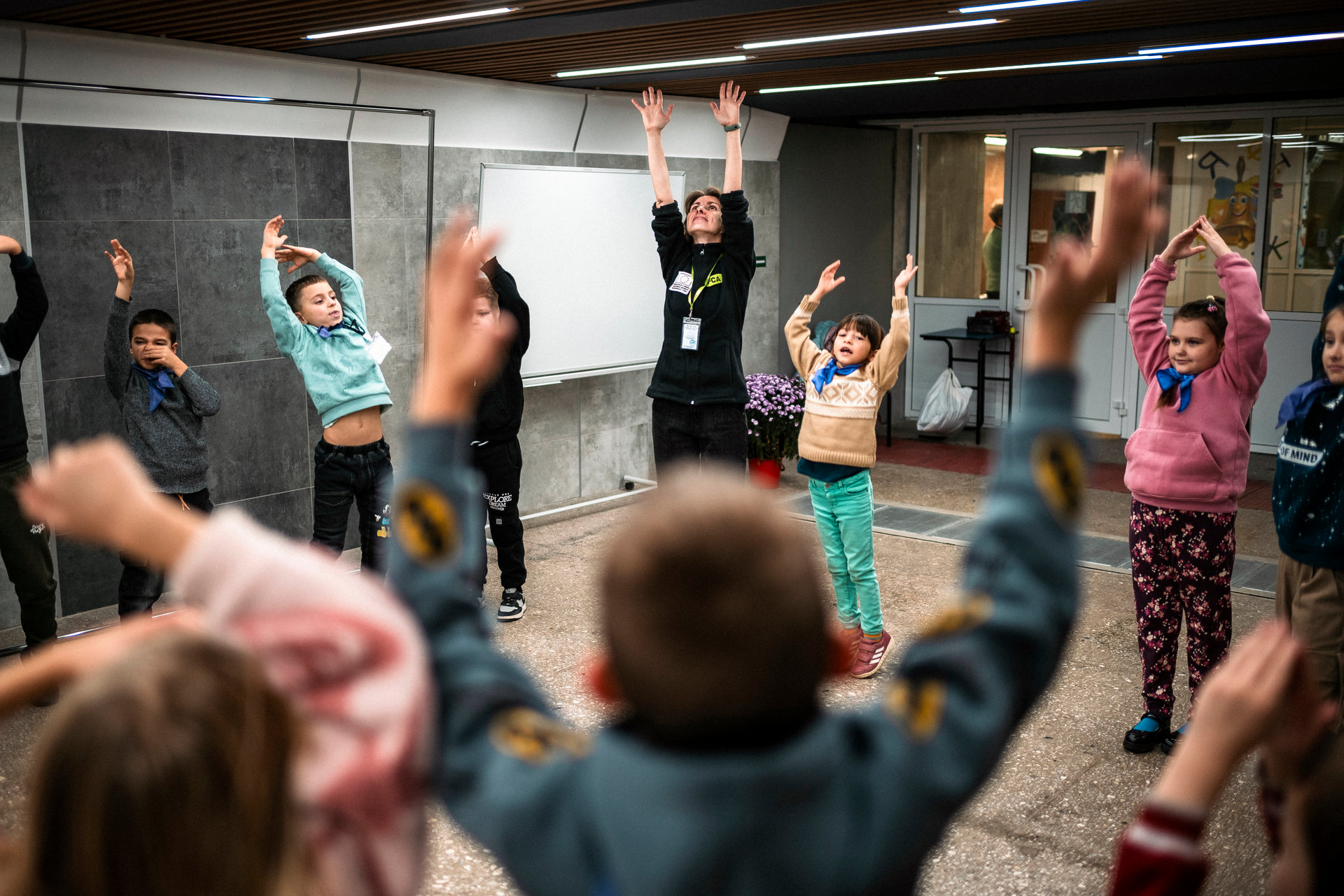 A group of children, led by a woman, stretch to the sky in an underground room.