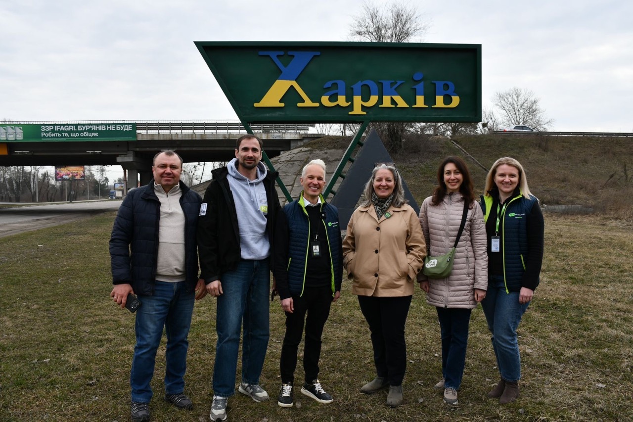 A group of people pose in front of a city sign for Kharkiv