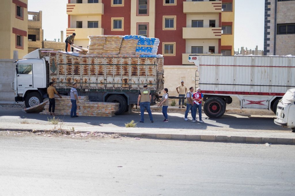 People around a truck, with a pile of mattresses on the bed.