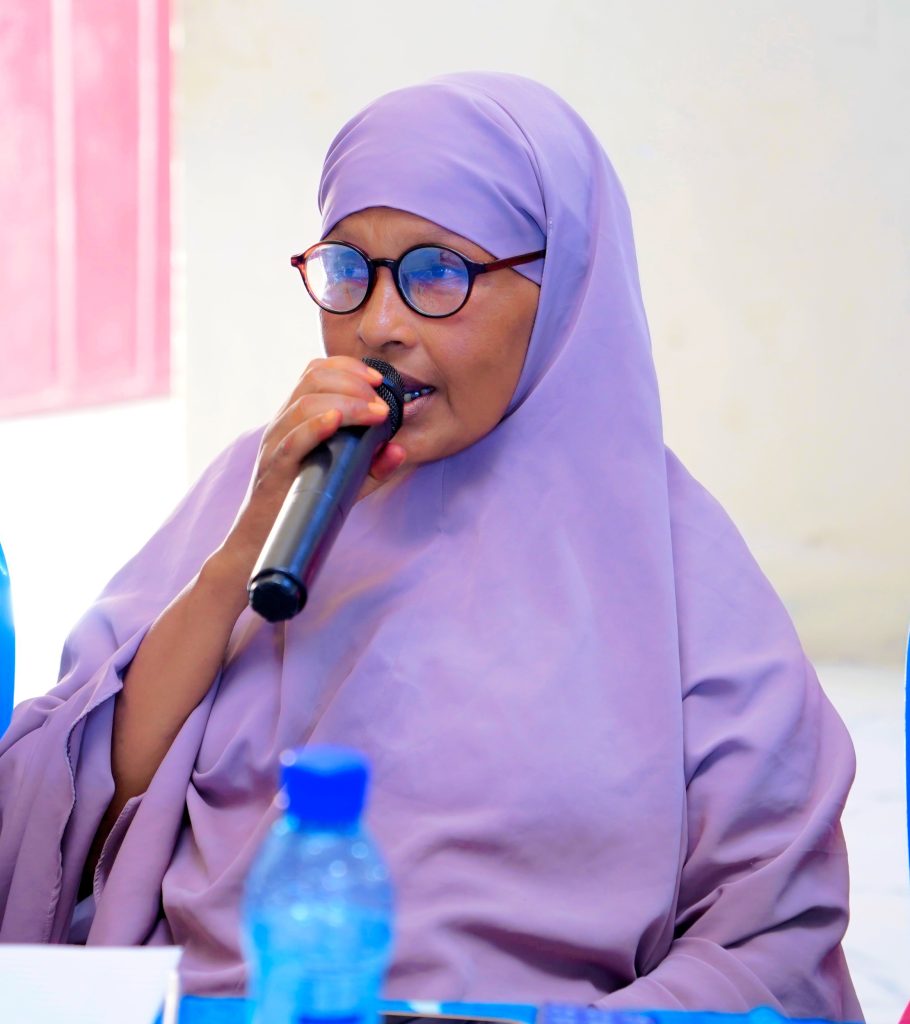 A woman in a purple hijab talks into a mic