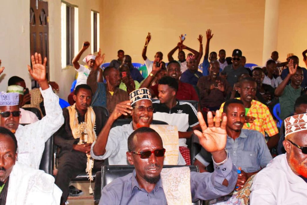Many people, mostly men, are sitting in a room and cheering with their hands up. 