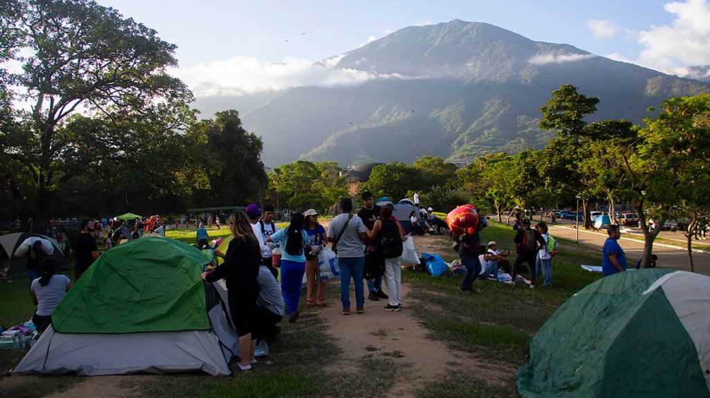 Ihmisiä ja telttoja Venezuelan maanjäristyksen jälkeen puistomaisessa ympäristössä. Taustalla näkyy korkeampi kukkula.