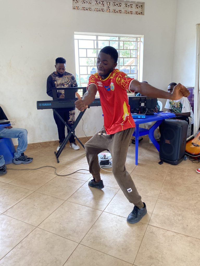 A man in a football shirt dances enthusiastically in a room while a man plays a keyboard in the background.