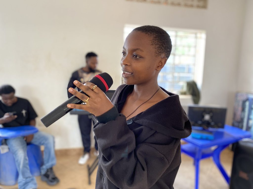 A woman in a black hoodie sings into a mic