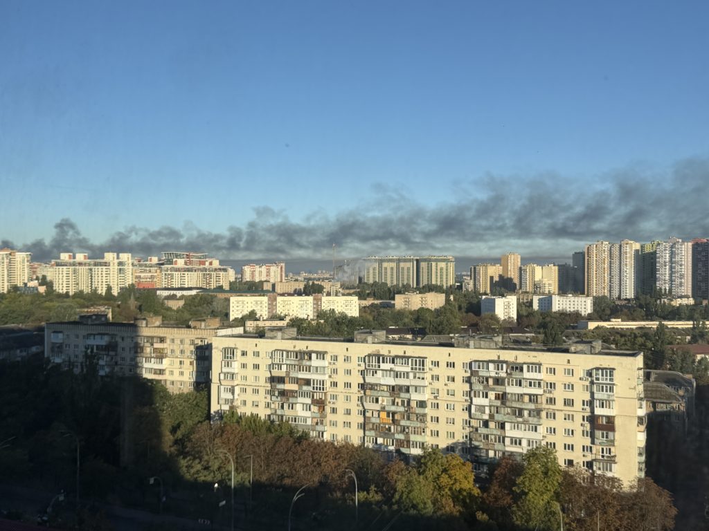 A city skyline. Smoke rises in the background.