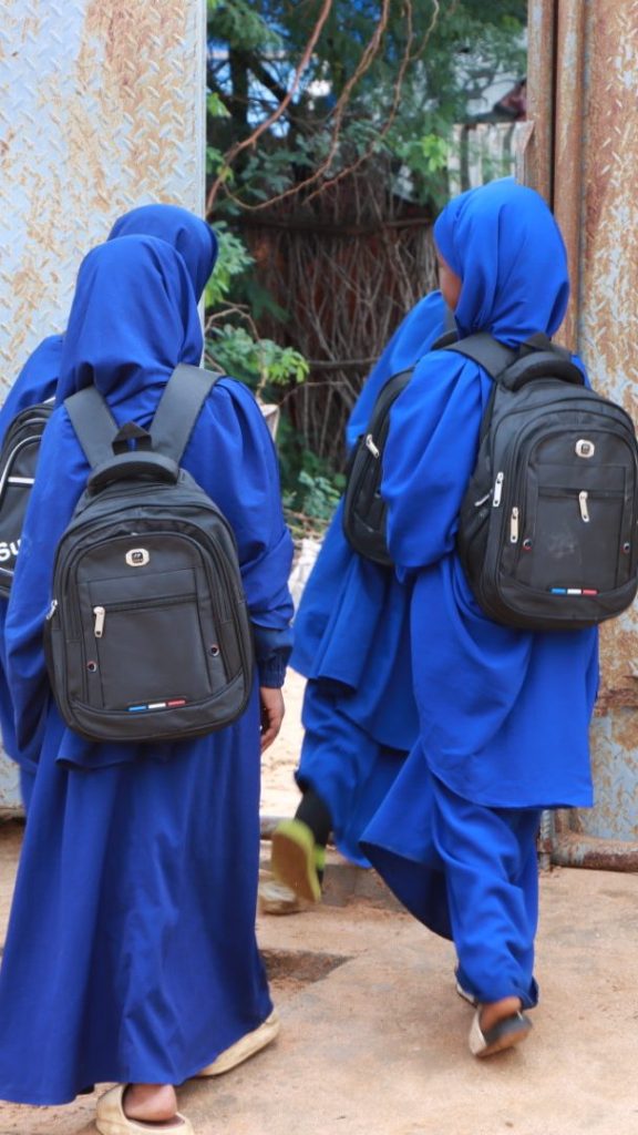 Four schoolgirls with backpacks leave a schoolyard through a door