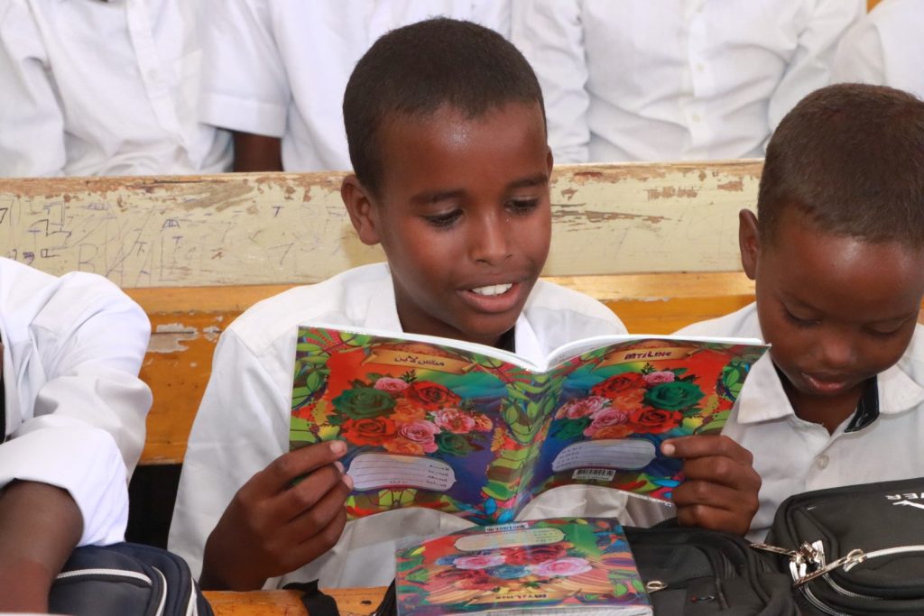 A schoolboy reads a book sitting at a desk beside a classmate